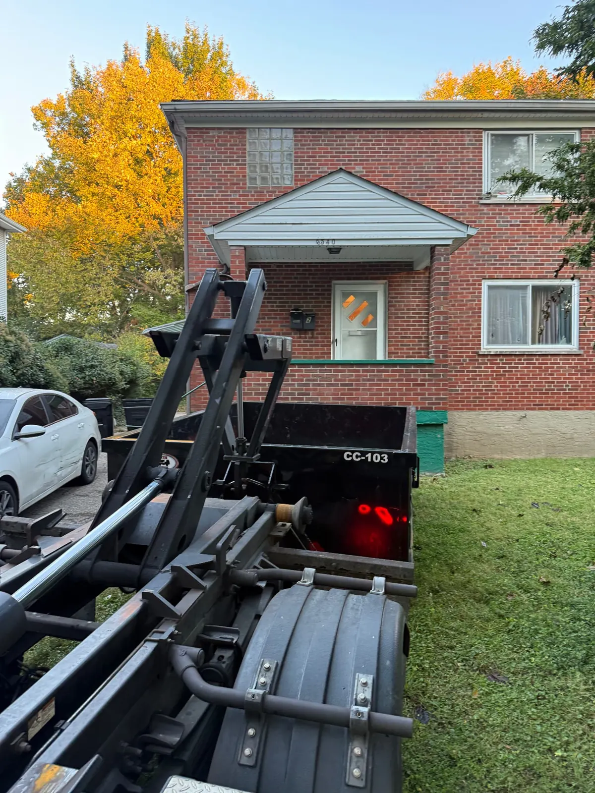 Clutter Cleanout 10 yard dumpster CC-103 with the roll-off truck on a driveway in front of a brick home in Cincinnati, OH