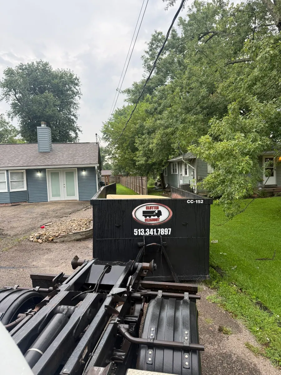 Clutter Cleanout 15 yard dumpster CC-152 being delivered from the roll-off truck to a Milford OH driveway between two homes