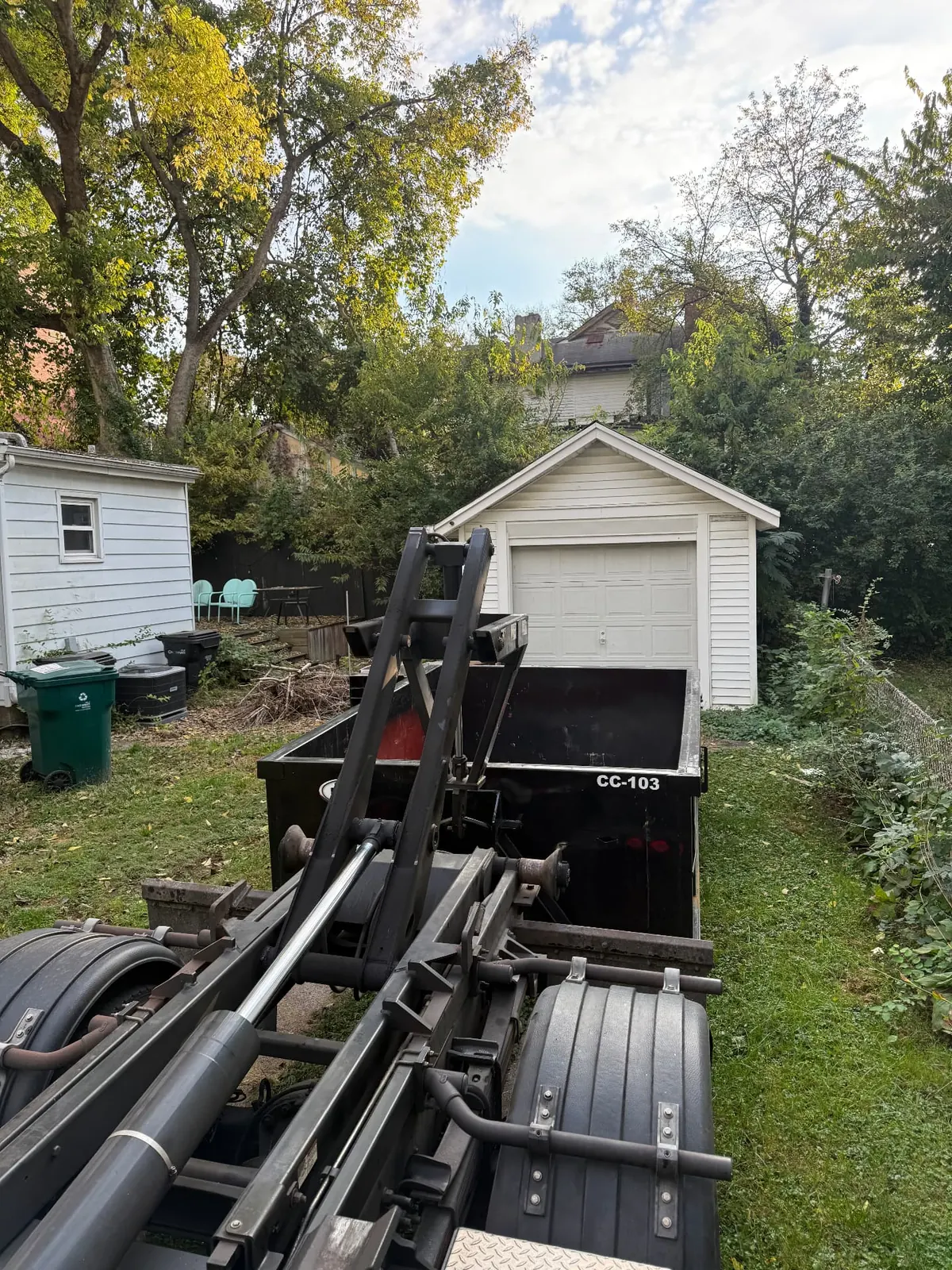 Clutter Cleanout 10 yard dumpster CC-103 on the hook-lift roll-off truck in a grassy backyard beside a white shed in Cincinnati, OH