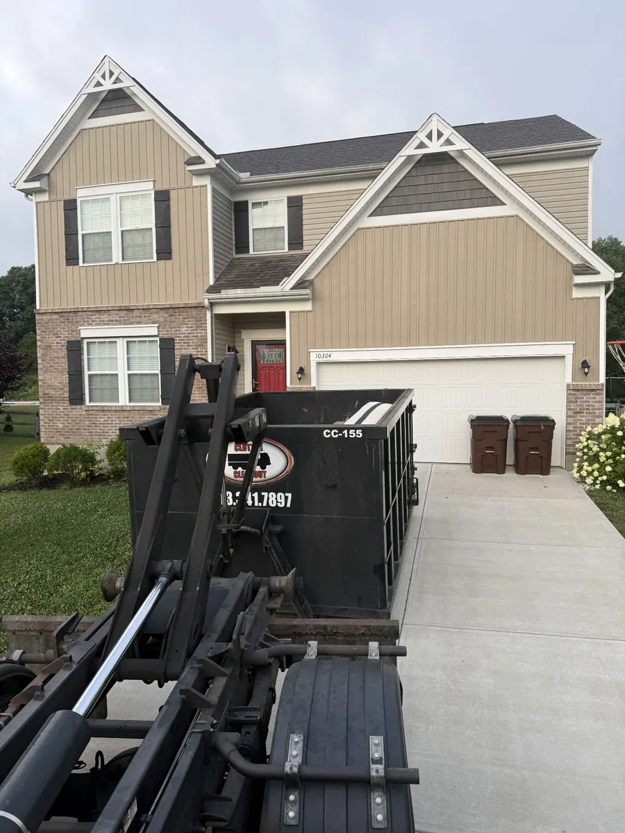 Clutter Cleanout 15 yard dumpster CC-155 delivered to a two-story tan Alexandria KY home driveway with roll-off truck in the foreground