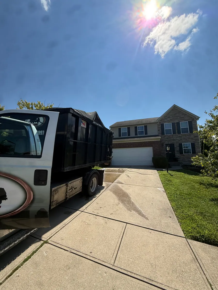 Clutter Cleanout roll-off truck delivering a tarped 15 yard dumpster to a Burlington KY driveway