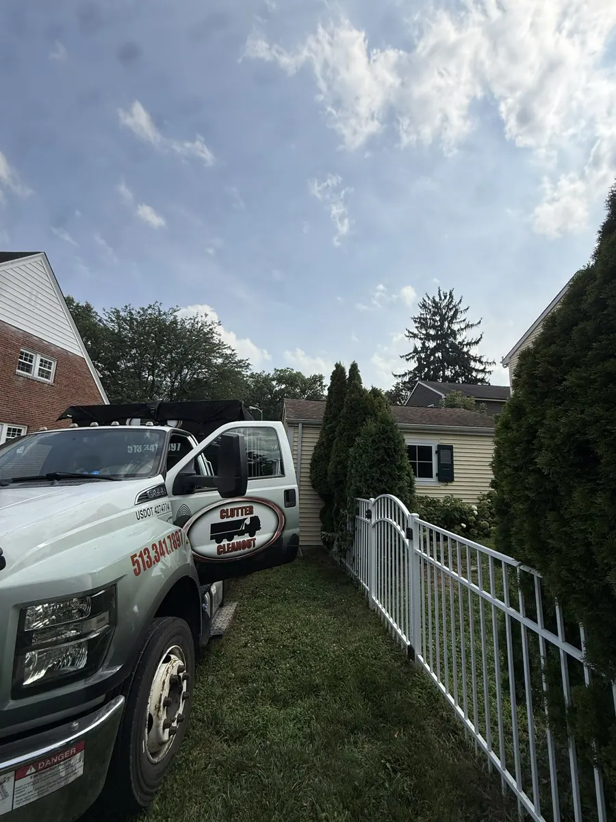 Clutter Cleanout roll-off truck CC-154 delivering a 15 yard dumpster along a narrow side yard in Mariemont, OH