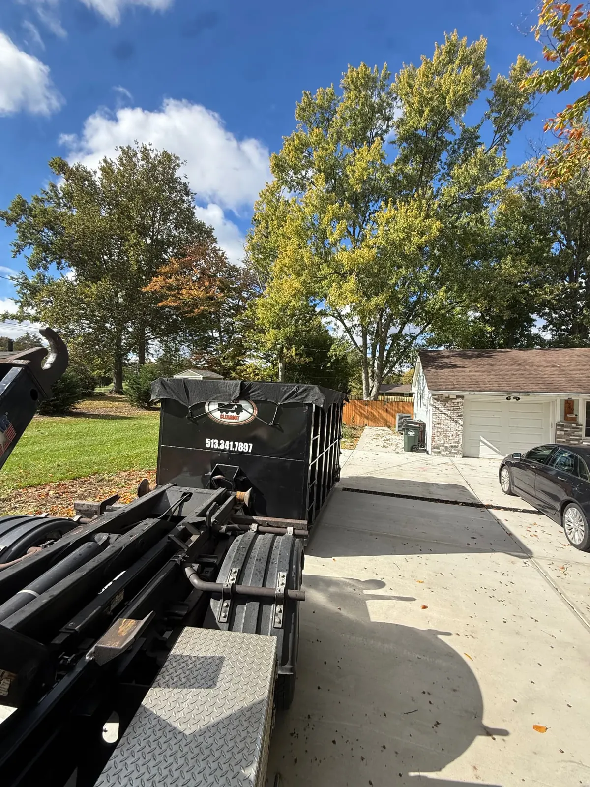 Clutter Cleanout tarped 20 yard dumpster with the roll-off truck on a residential driveway beside a garage in Amelia, OH