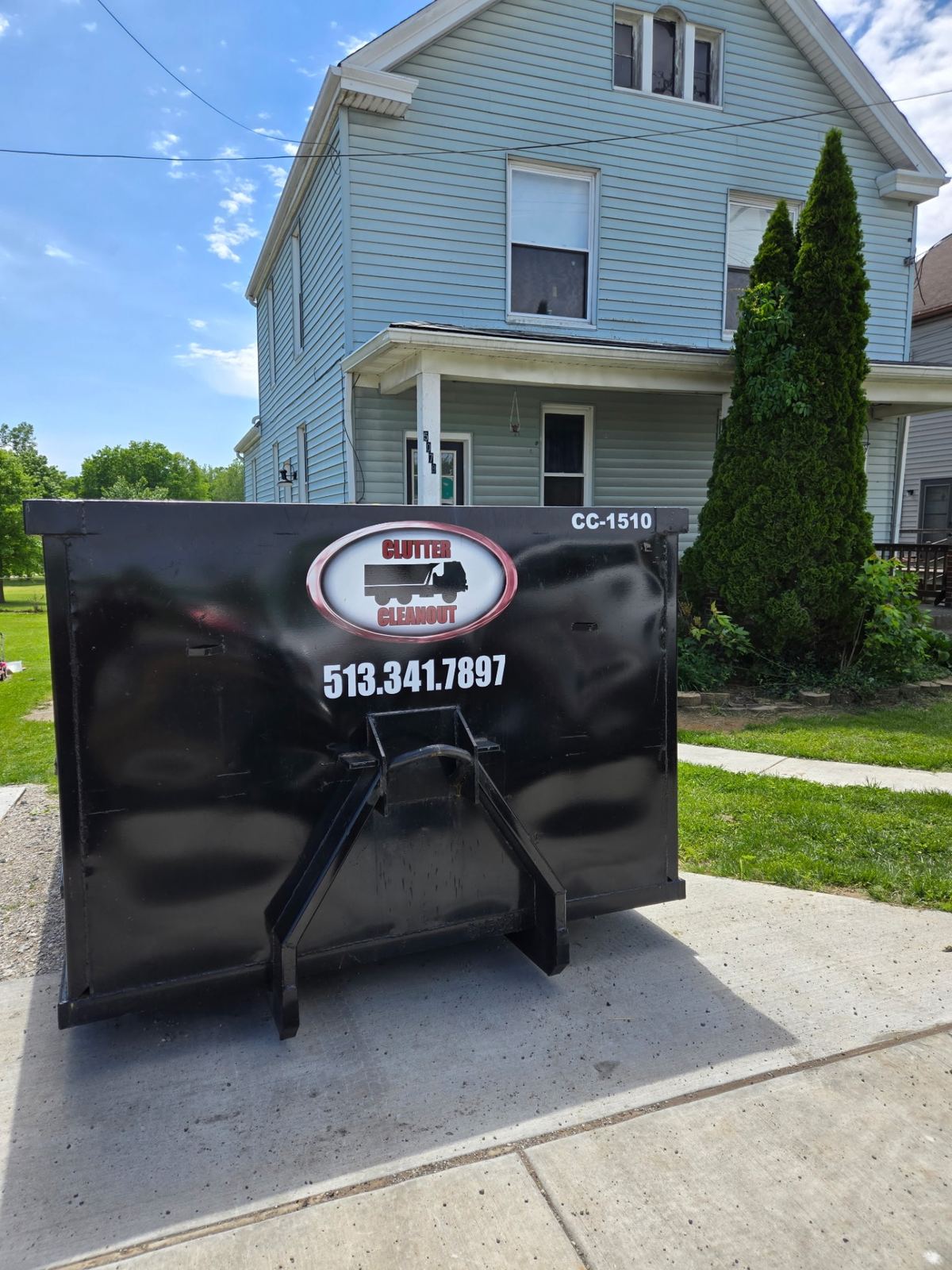 15-yard Clutter Cleanout dumpster CC-1510 placed on a driveway in front of a blue two-story home in Alexandria, KY