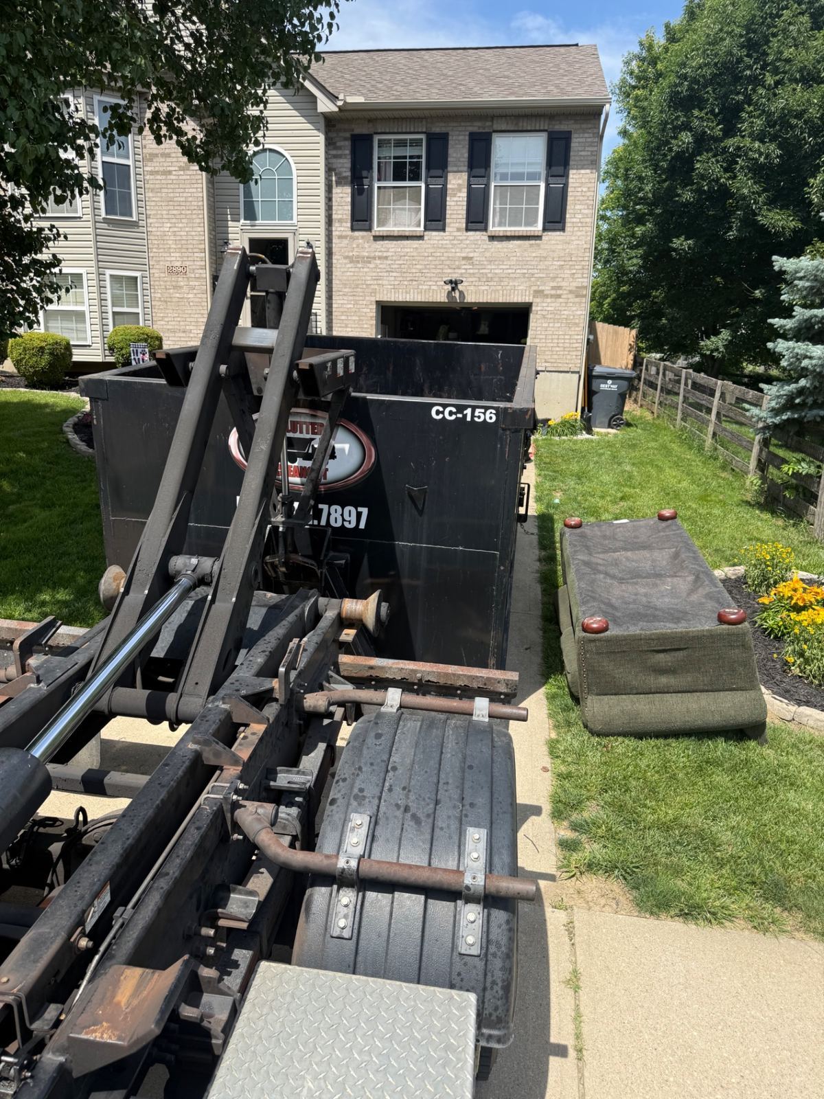 Clutter Cleanout 15 yard dumpster CC-156 being dropped off at a Hebron KY home for a house cleanout, with an old couch on the lawn ready to load