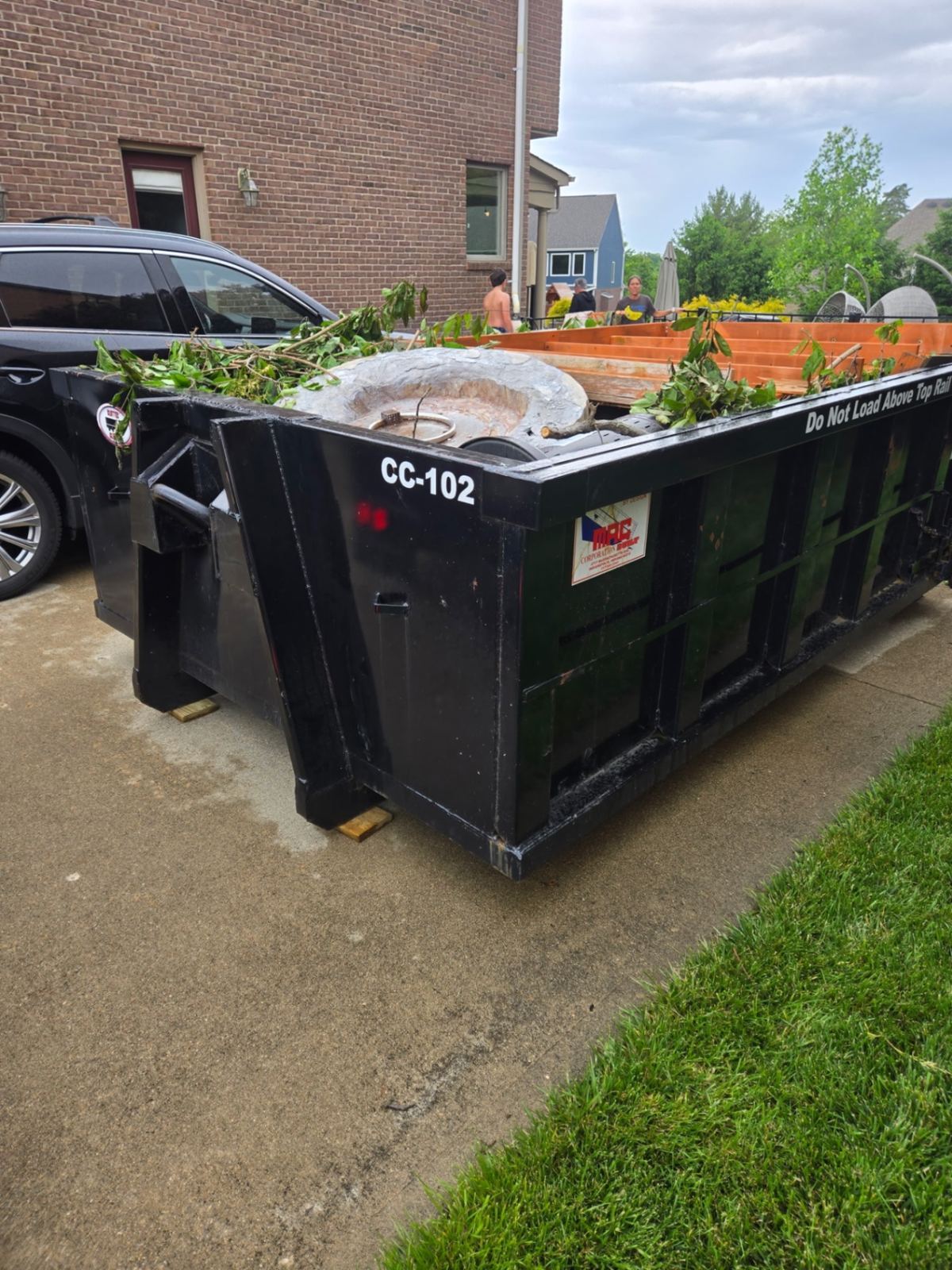 Clutter Cleanout 10 yard construction dumpster CC-102 loaded with a concrete fire pit, framing lumber, and brush on a Loveland OH driveway