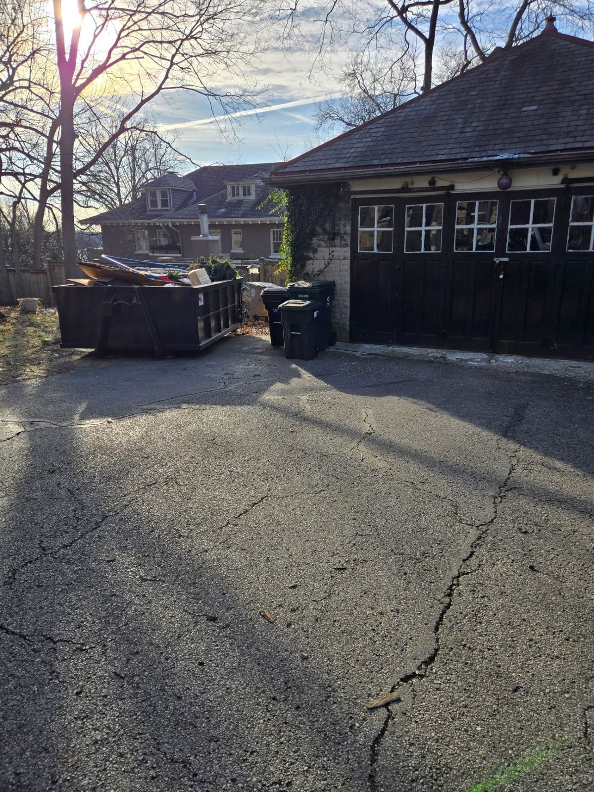 Clutter Cleanout dumpster loaded with junk next to a garage during a Montgomery OH home cleanout